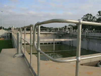 Water treatment facility with metal hand railings and sedimentation tanks under a cloudy sky.