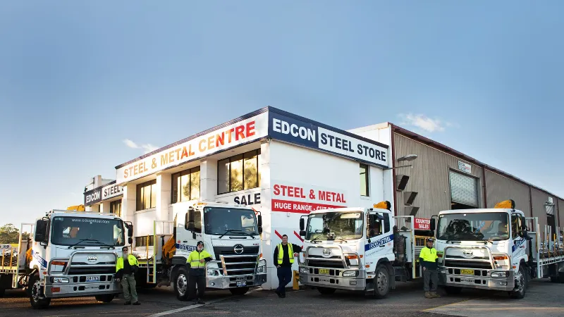 Edcon Steel delivery trucks parked in front of the Edcon Steel & Metal Centre building, with staff standing beside them.
