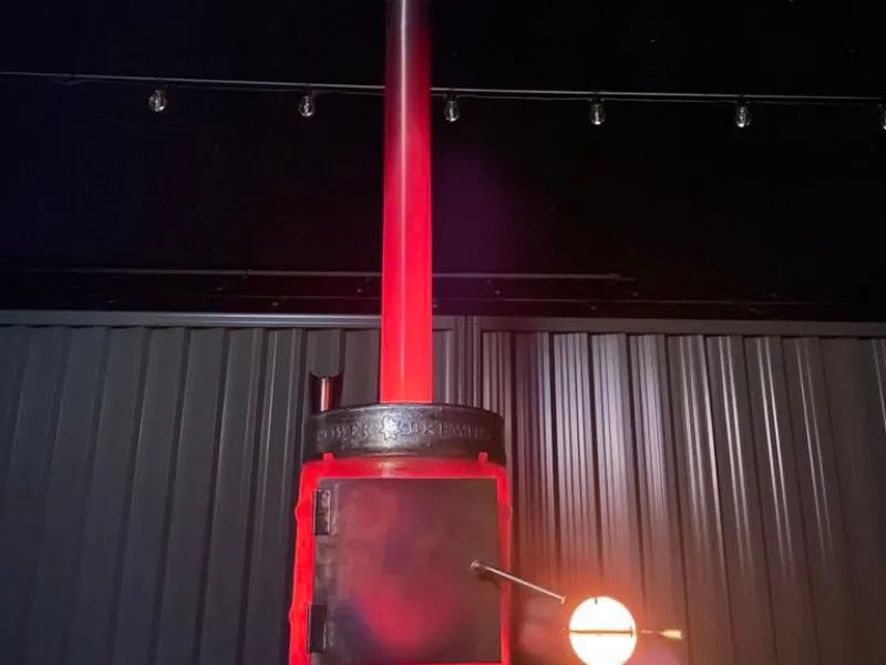 A tall, red rocket-style outdoor heater glowing against a dark background inside a metal-clad space.