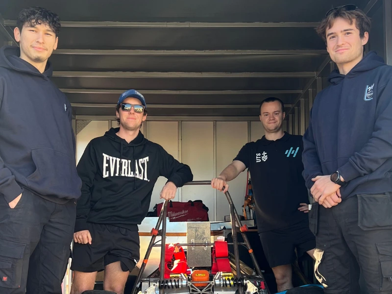 Four UTS Motorsports team members standing proudly around a race car frame inside a trailer.