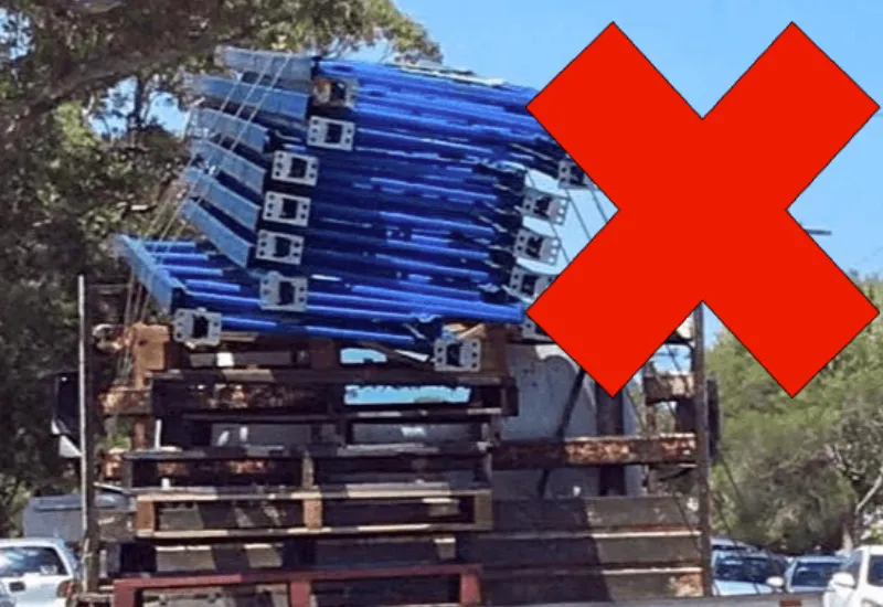 Unsafe transport of stacked steel frames on truck with unsecured and leaning load marked with a red cross
