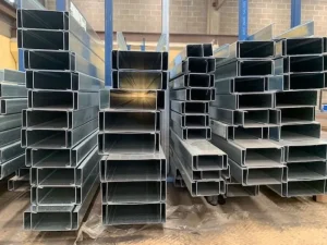 Stacks of hollow steel rectangular tubing in a warehouse, stored in organized piles on the floor and pallets
