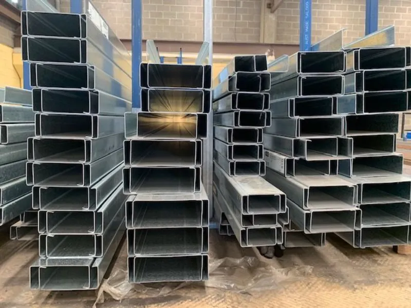 Stacks of hollow steel rectangular tubing in a warehouse, stored in organized piles on the floor and pallets