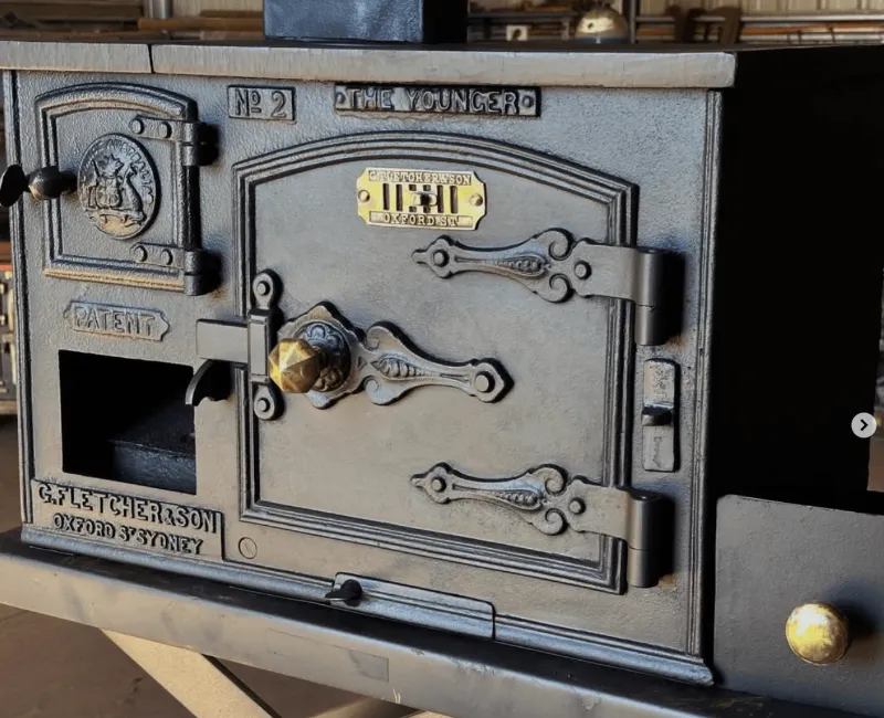 Close-up of restored The Younger No.2 oven door with brass plate and ornate hardware.