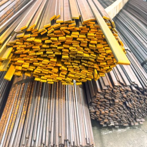 Stack of yellow-painted metal rectangular bars bundled for transport in an outdoor yard with more bars in the background.