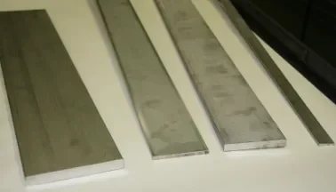 Various shapes, weights, sizes of steel flat bar sitting side by side on table.