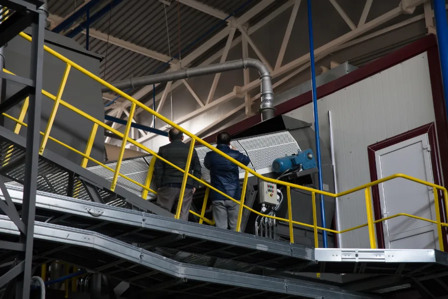 Two factory workers examine machine on elevated platform with handrail