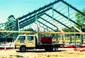 Steel-framed building under construction with a white van labeled EDCON STEEL in the foreground.