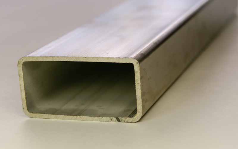 Rectangular hollow steel tube with open ends resting on a light surface, brushed metal finish